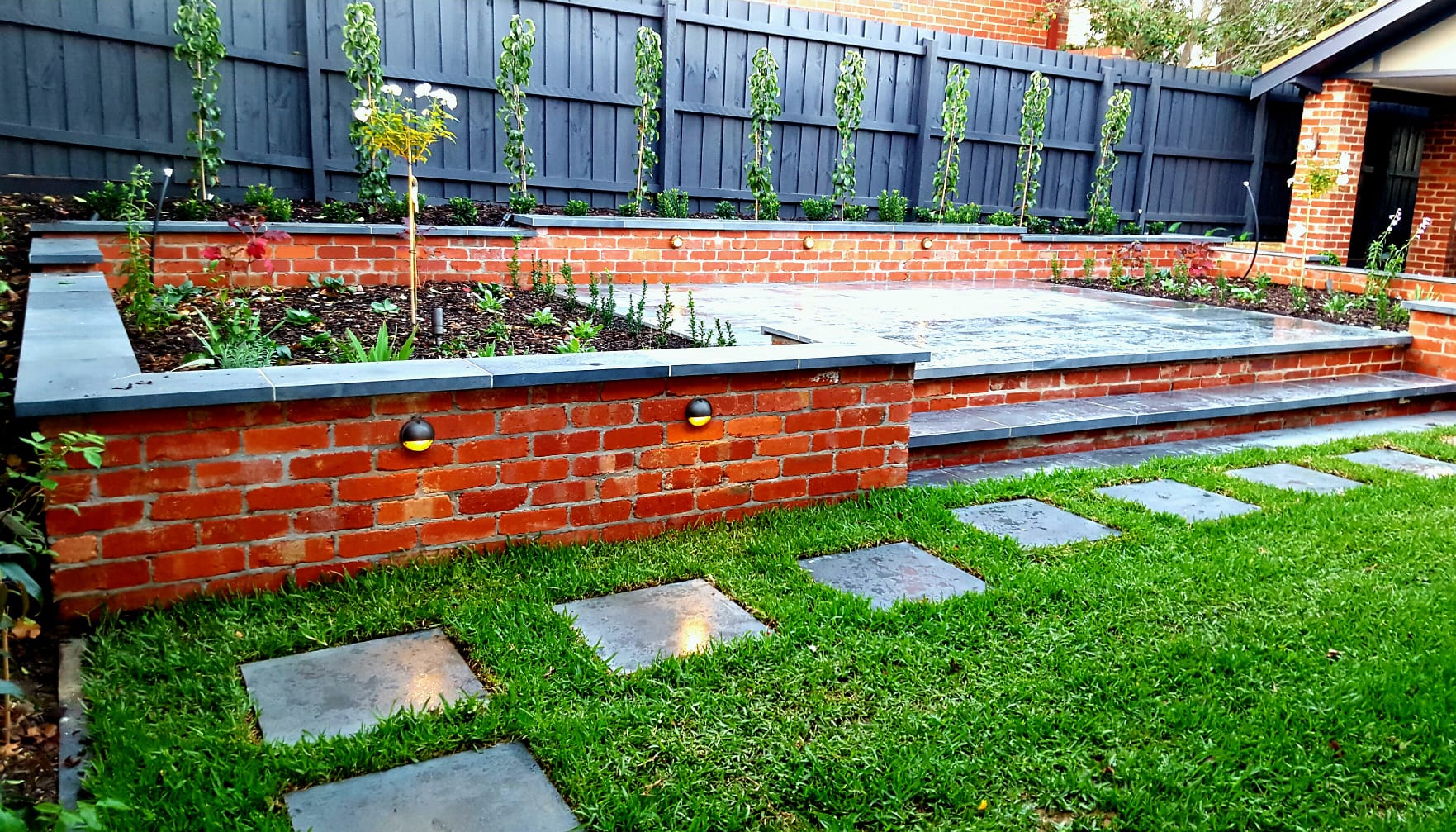 Completed premium garden with brick retaining walls, bluestone paving and lawn